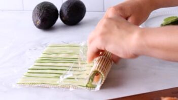 Rolling sushi with a bamboo mat. Avocados in the background.