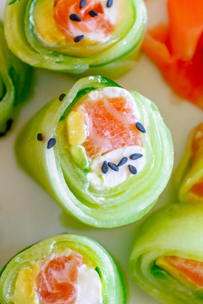 Close up of salmon Philadelphia sushi roll wrapped in cucumber and topped with sesame seeds.