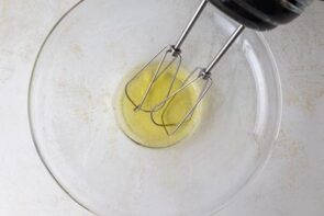 A clear bowl with egg whites and a handheld electric mixer ready to whip.