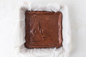 Freshly baked brownies in a parchment-lined square pan with a crackly top.