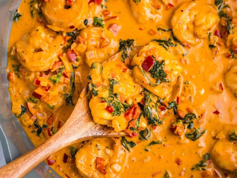 A wooden spoon holding a serving of creamy shrimp