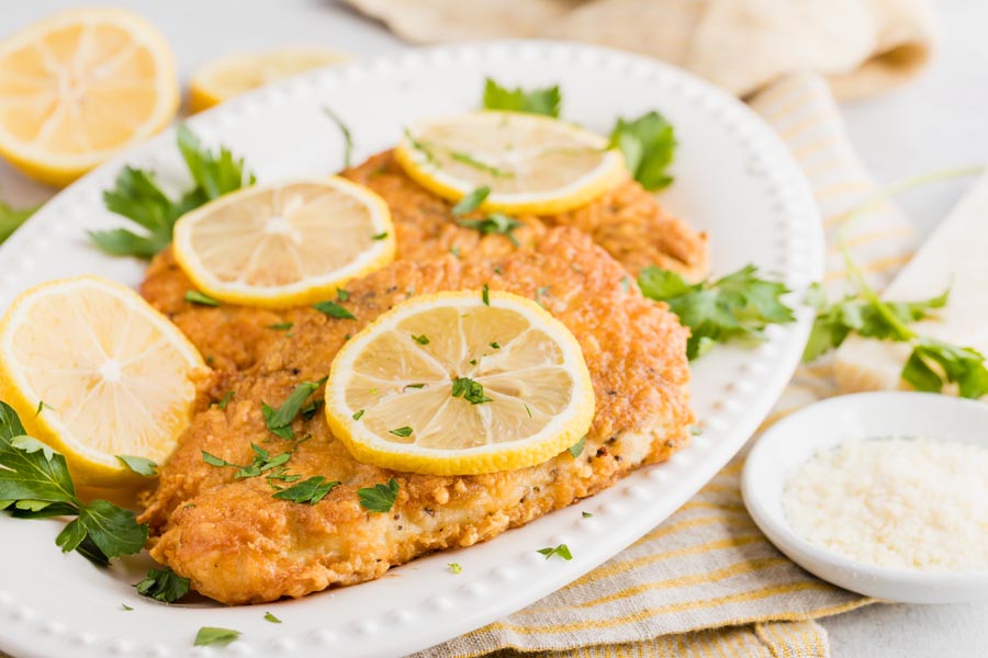 crispy parmesan crusted chicken cutlets on a serving platter topped with lemon