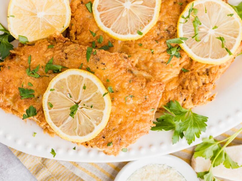 chicken cutlets breaded with parmesan cheese and fried are on a white plate with parsley and lemon