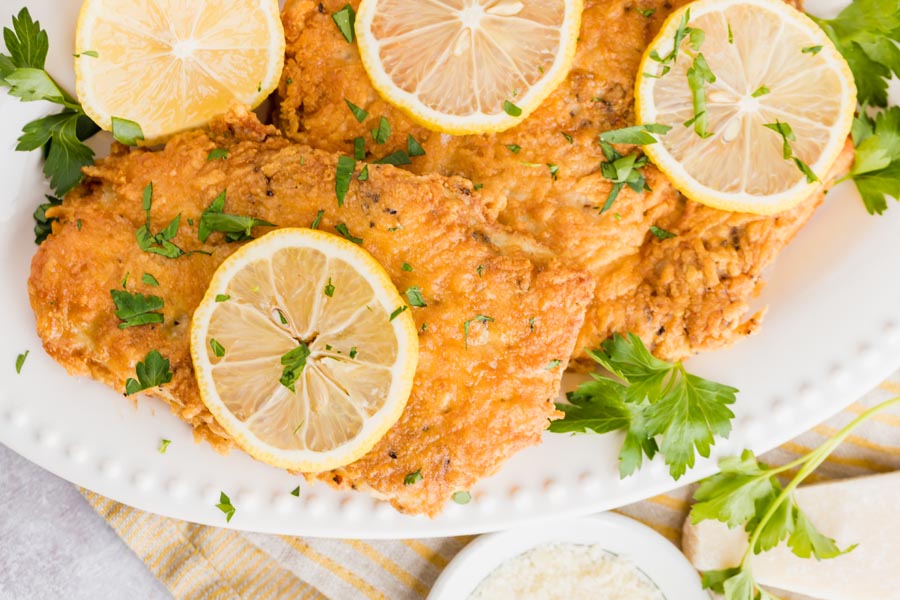 chicken cutlets breaded with parmesan cheese and fried are on a white plate with parsley and lemon