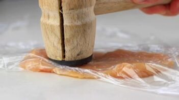 hammering chicken breast into a thin sheet covered in plastic wrap