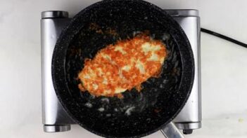 frying a cheese coated chicken cutlet in a skillet with oil