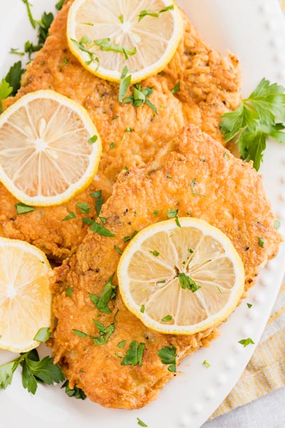 two pieces of crispy fried chicken on a platter topped with lemon and parsley leaves