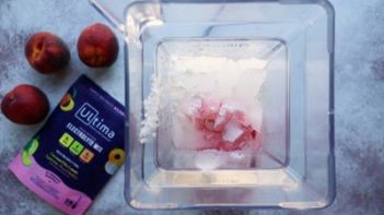 a blender with ice and cocktail ingredients in it with peaches near by