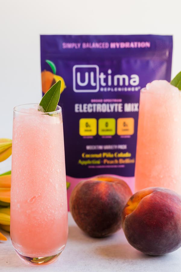 two bellini cocktails with peaches and a bag of ultima behind them