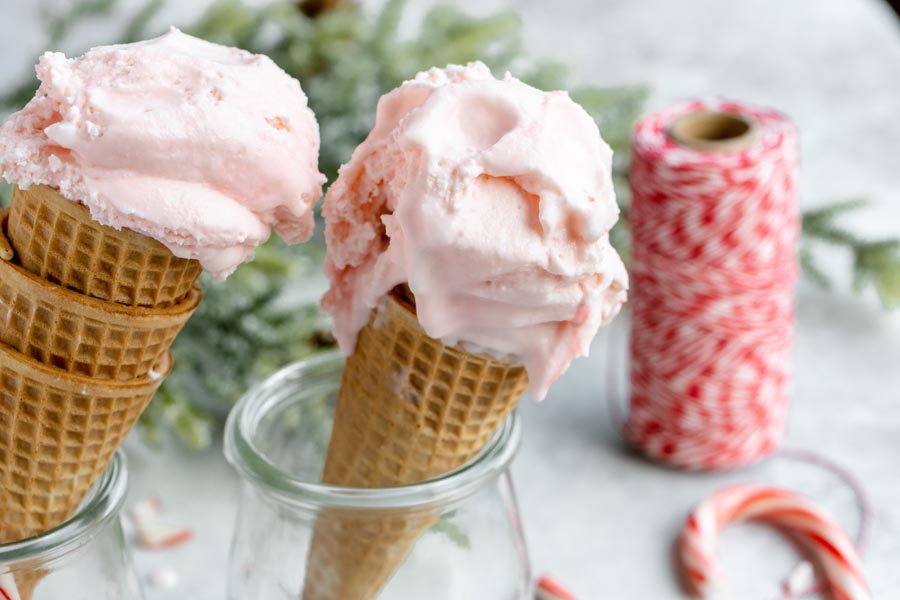 pink ice cream scooped into cones with red thread and a candy cane in the background