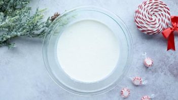 a bowl with white ice cream base in it next to a large peppermint candy