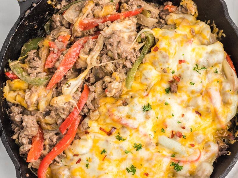 A cheesey casserole in a skillet, half covered with melted cheese the other with the cheese mixed in.