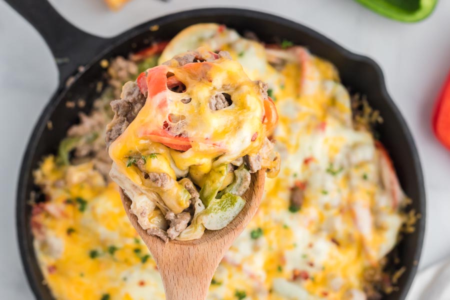 A wooden spoon holding a spoonful of cheesy philly cheesesteak casserole.