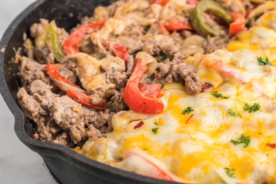 A beef and pepper casserole in a skillet with half covered in melted cheese.