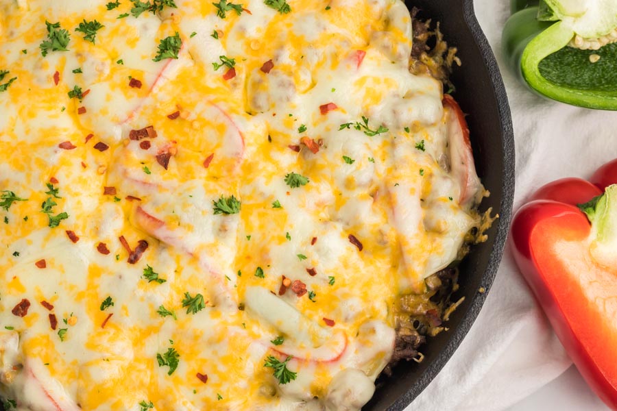 A melted cheese covered skillet casserole dish with sliced red and peppers around.