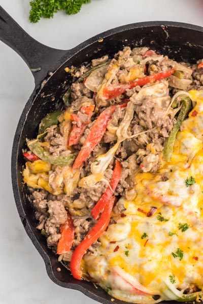 Philly cheesesteak casserole with ground beef, red and green bell peppers in a skillet, half covered in melted cheese.