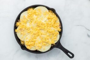 Sliced provolone cheese and shredded cheese in a cast iron skillet.