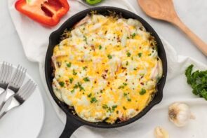 A melted cheese covered casserole in a skillet with ingredients nearby.