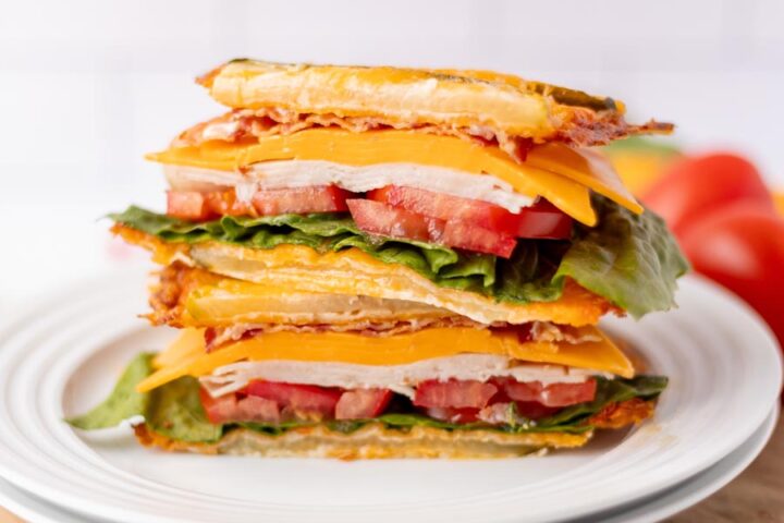 A stacked sandwich made with crispy cheese bread, turkey, cheddar cheese, lettuce, and tomato slices.