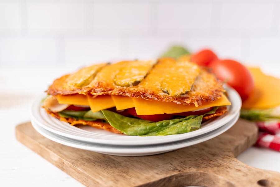 A low-carb sandwich with layers of turkey, cheddar, lettuce, and tomato between baked cheese and pickle 