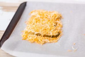 Pickle slices covered with shredded cheese on a baking sheet ready to be baked.