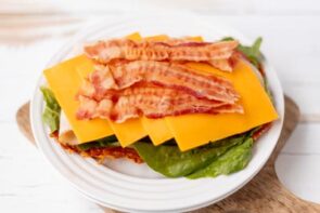 A plate stacked with bacon, cheddar cheese, turkey, and lettuce ready to assemble the sandwich.