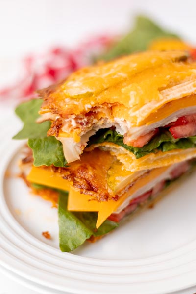 A sandwich with a bite taken out, showing the crispy cheese, turkey, lettuce, and tomato layers.