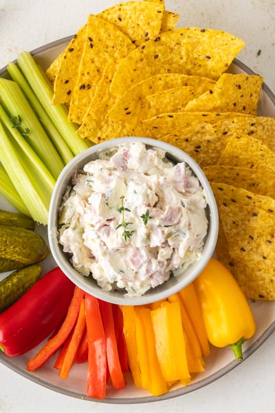 Pickle wrap dip served on an appetizer platter with tortilla chips, celery sticks, bell peppers, and whole pickles.