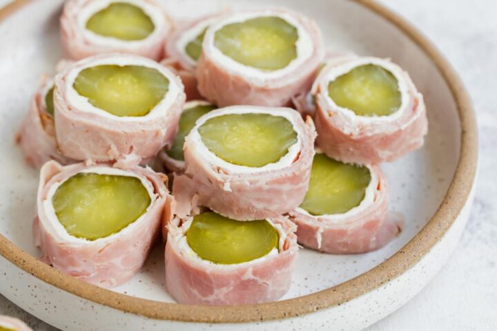 A plate full of pickle roll-ups wrapped in deli meat with a cream cheese layer.