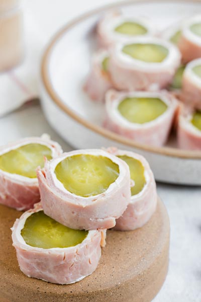 Close-up of pickle roll-ups with cream cheese and ham stacked on a small wooden pedestal.