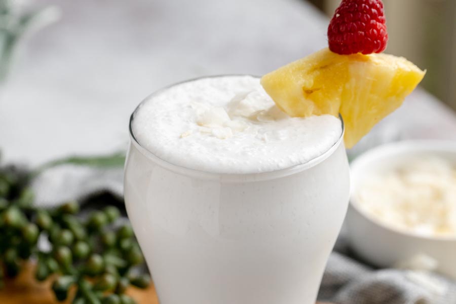 a frothy white smoothie topped with a pineapple wedge and a raspberry
