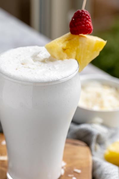 a pina colada smoothie in a glass with a pineapple and raspberry garnish
