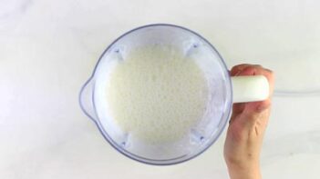 a milk looking smoothie inside a blender with a hand holding the blender