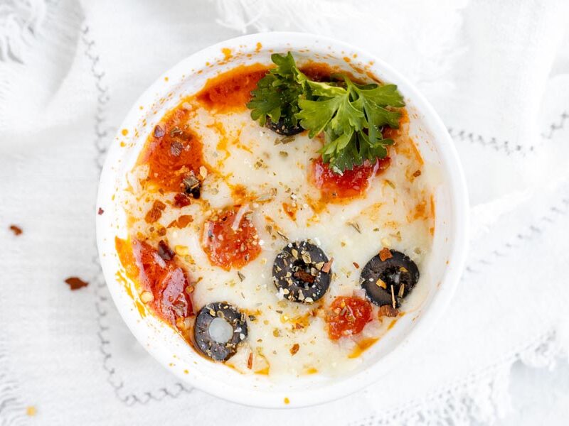 looking down onto a bowl with pizza in it and slices of pepperoni and olives