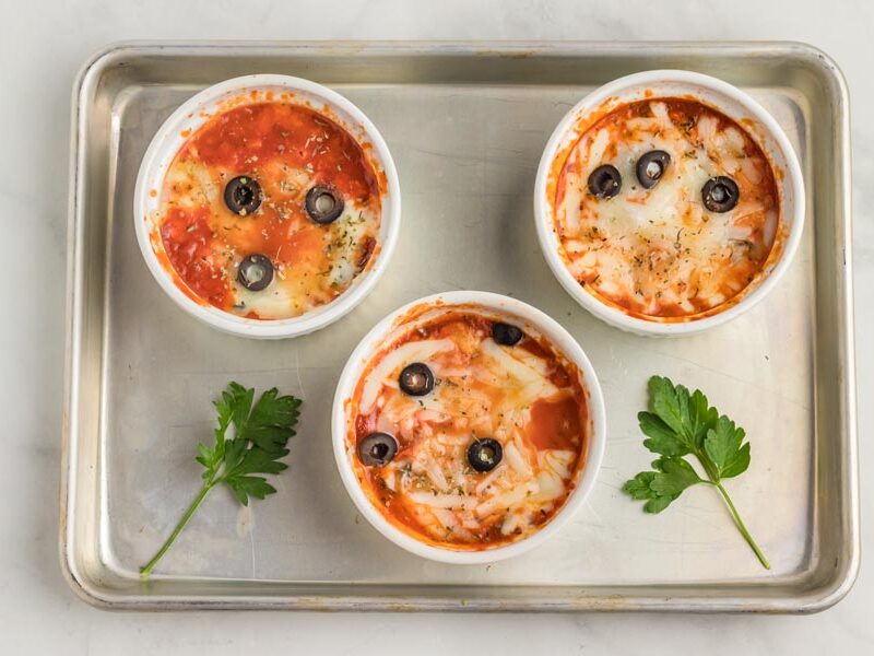 Three white ramekins filled with pizza toppings and melted cheese on a baking tray.