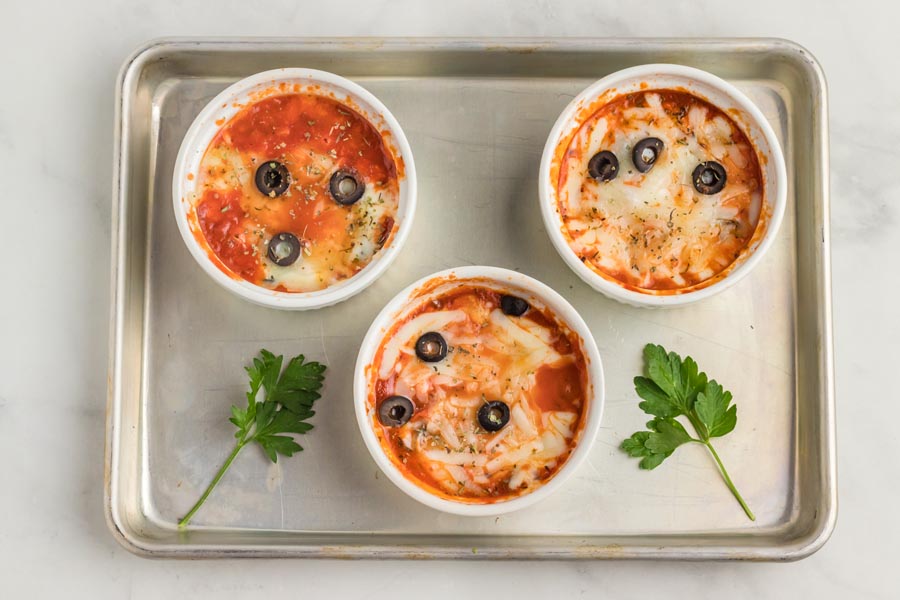 Three white ramekins filled with pizza toppings and melted cheese on a baking tray.