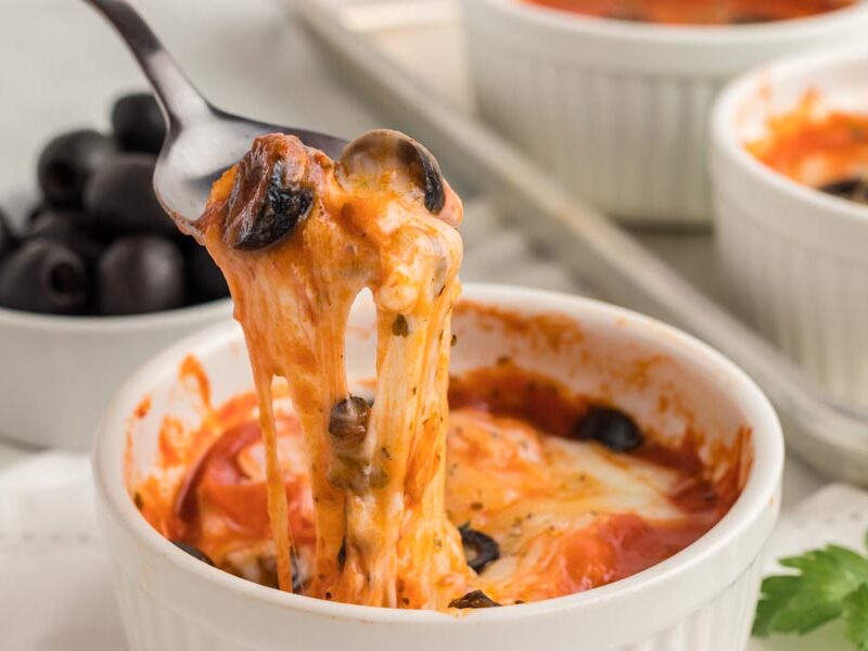 A spoon pulling melted cheese and sauce from a pizza bowl.