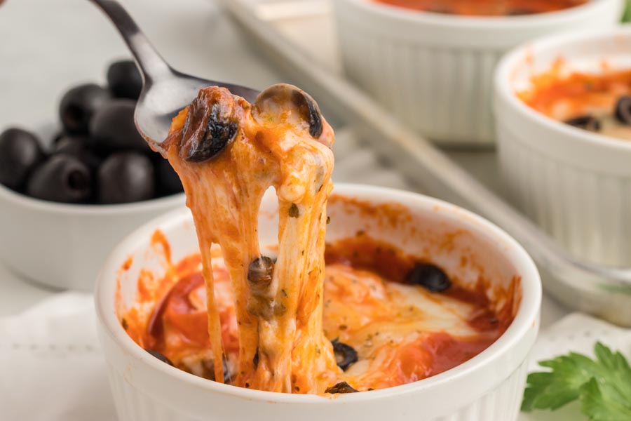 A spoon pulling melted cheese and sauce from a pizza bowl.