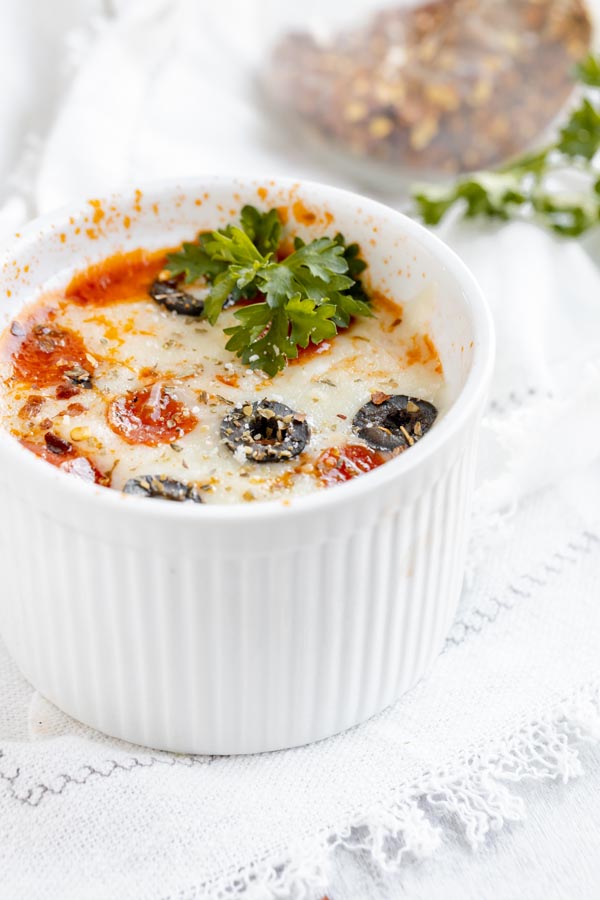 a large ramekin with a pizza cooked inside topped with parsley and olives