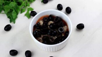 olives and crumbled sausage in a ramekin with black olives sprinkled around