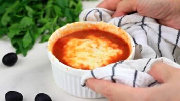 holding a small ramekin with melted cheese and marinara sauce with a towel