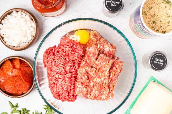 ground beef and ground pork in a bowl with an egg and other ingredients near by