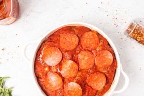 pepperoni slices over marinara sauce in a casserole dish