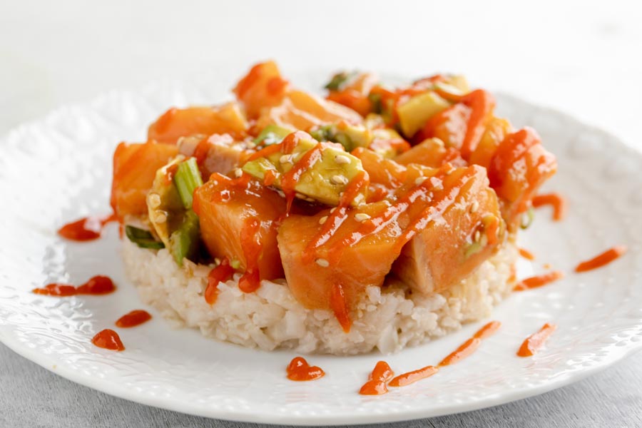 a plate with poke over rice and topped with sriracha sauce