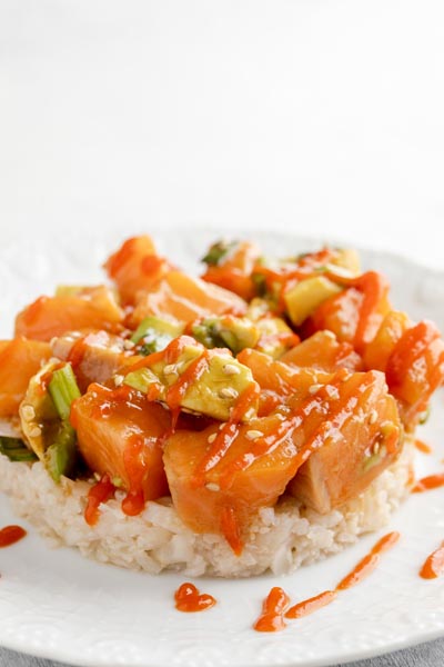 salmon and rice stacked on each over on a white plate with red sauce all over
