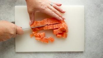 cutting raw salmon on a cutting board with a knife