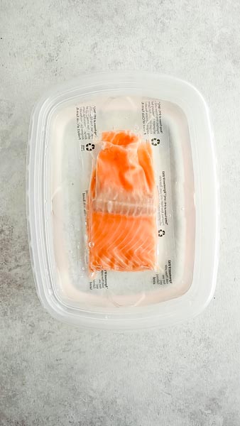 a package of salmon fillet thawing in a plastic container filled with water