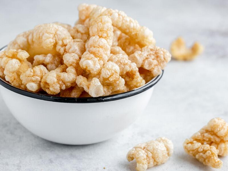 An enameled bowl with freshly fried pork rinds and a couple of pork rinds on the counter.