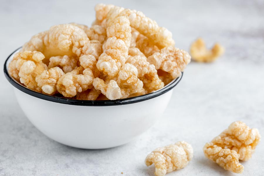 An enameled bowl with freshly fried pork rinds and a couple of pork rinds on the counter.