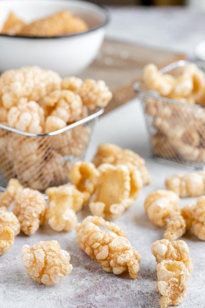 Crunchy pork skins on a table next to two small baskets with filled with more pork rinds.